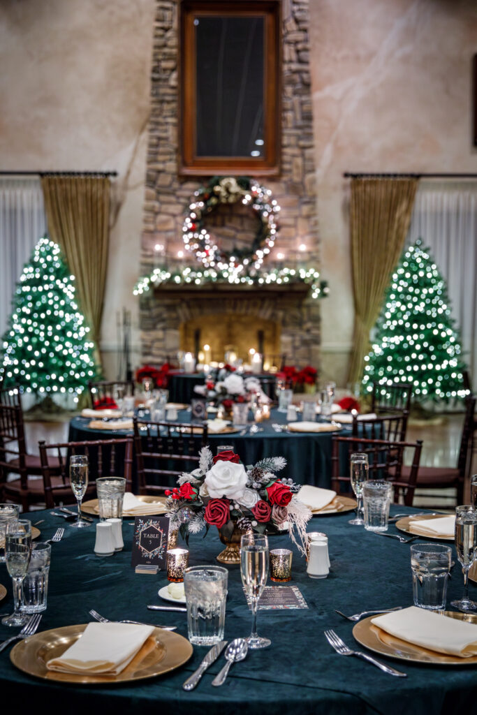 Elegant holiday table setting in front of a decorated fireplace, with Christmas trees and a festive wreath.