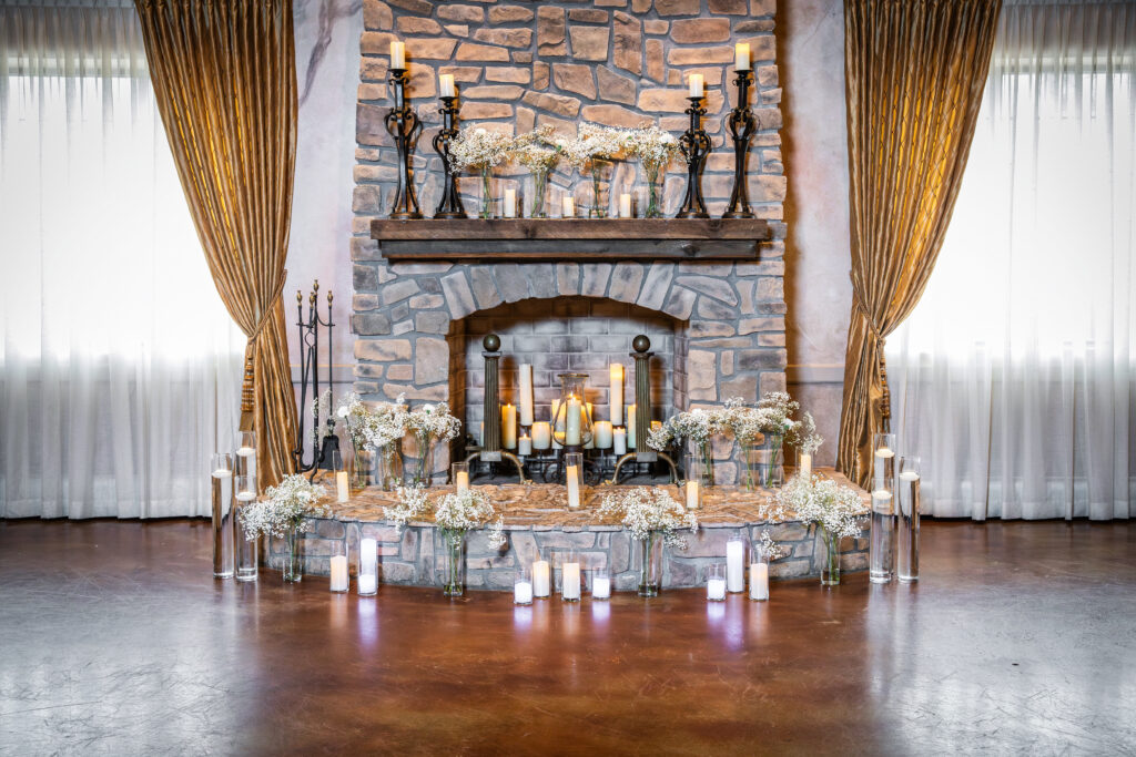Elegant fireplace with candles, flower arrangements, and sheer curtains, creating a cozy, romantic ambiance.