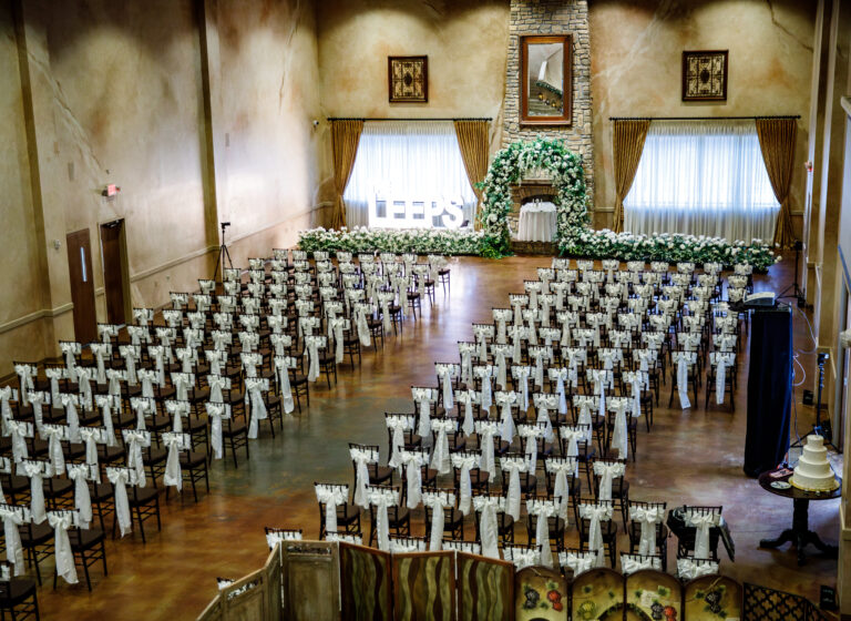 Wedding ceremony setup with rows of chairs draped in white, a floral arch, and 