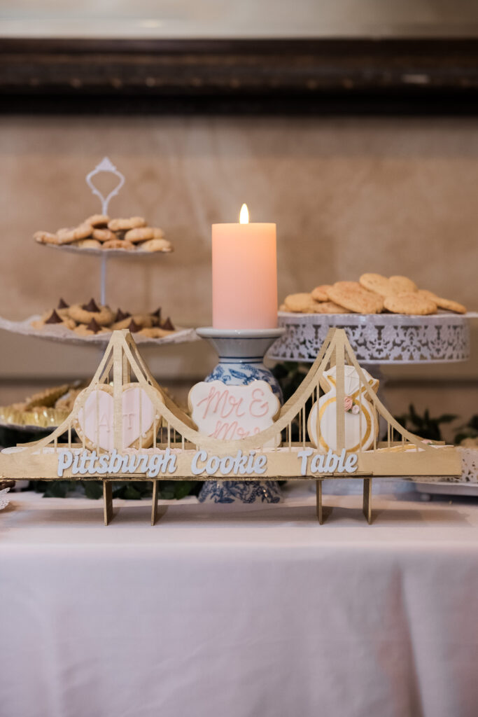 Table with cookies on stands, a lit candle, and a decorative bridge sign labeled "Pittsburgh Cookie Table.