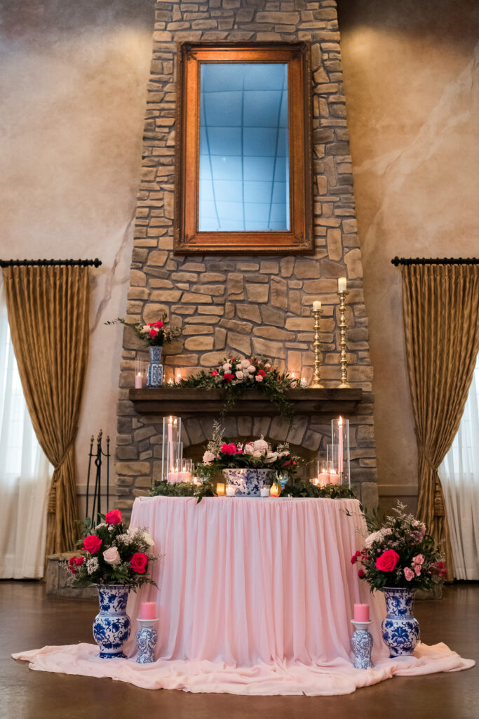Elegant stone fireplace centerpiece with tall mirror, floral arrangements, candles, and draped pink tablecloth.