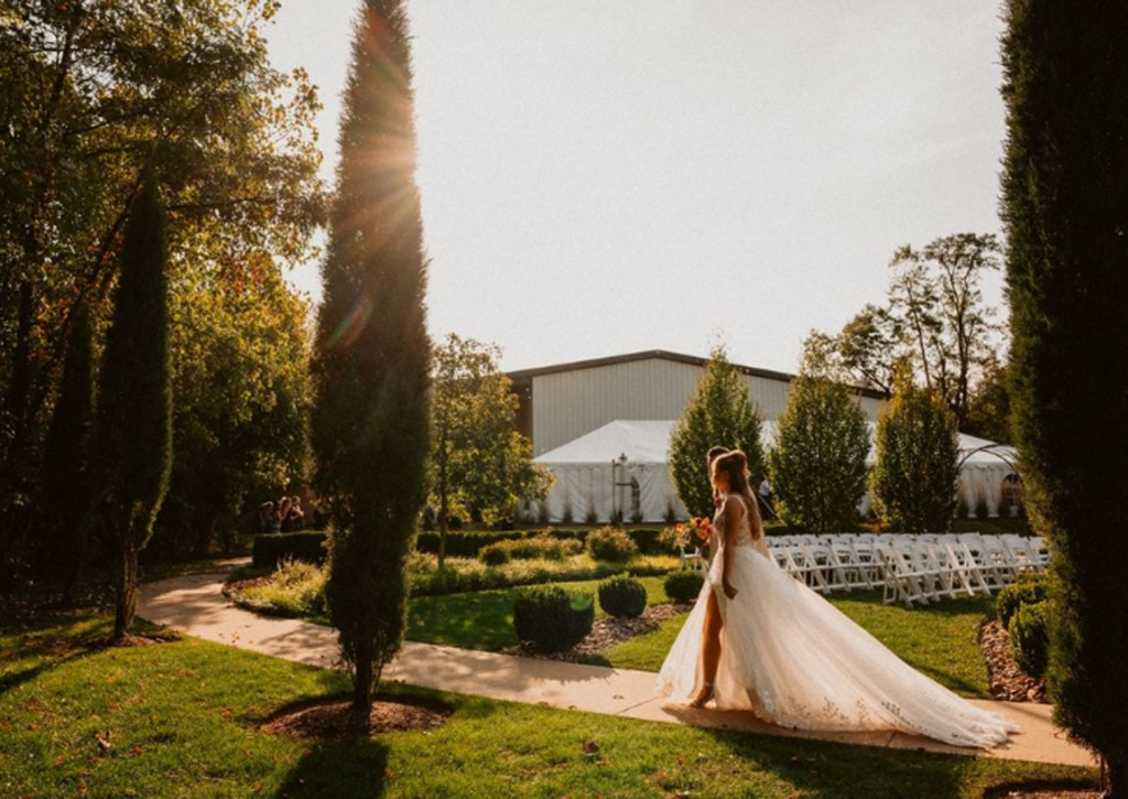 Bride walking on a garden path, with a long train, near a wedding venue in the late afternoon sun.