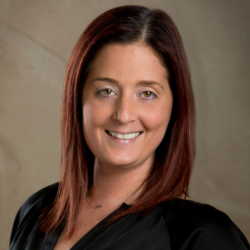 Smiling person with straight, dark auburn hair wearing a black top against a neutral background.