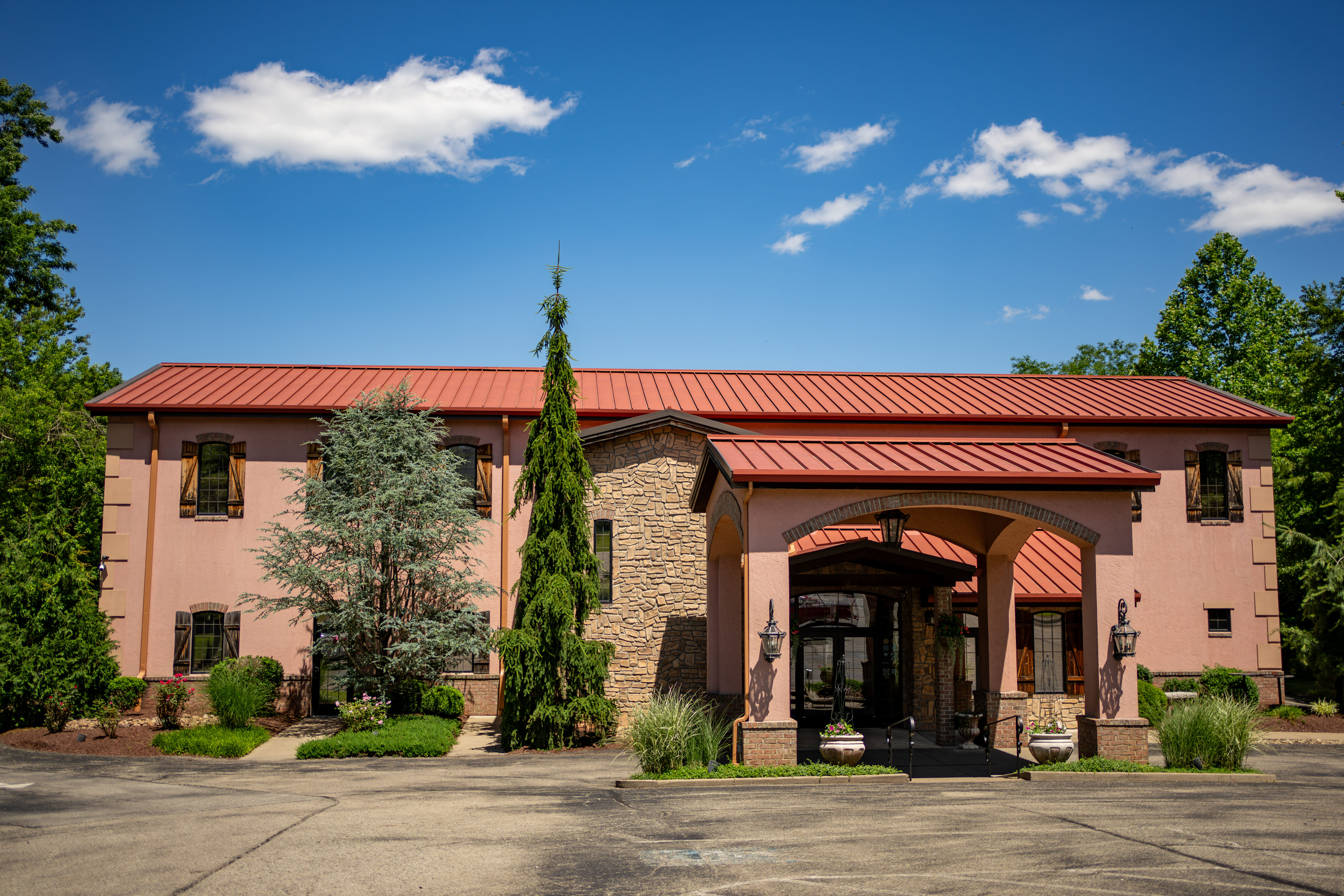 A two-story building with a red roof, entrance archway, and surrounding trees against a blue sky.
