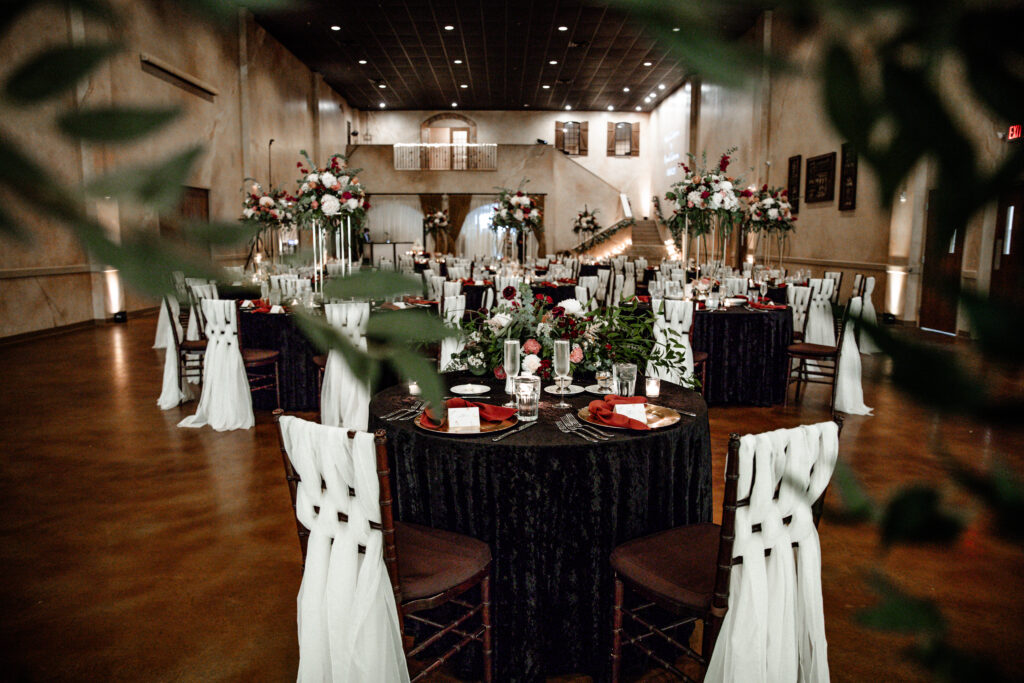 Elegant wedding reception with round tables, white chair covers, floral centerpieces, and a wooden floor.