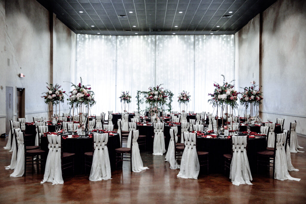 Elegant wedding reception with round tables, floral centerpieces, and chairs draped in white fabric in a decorated hall.
