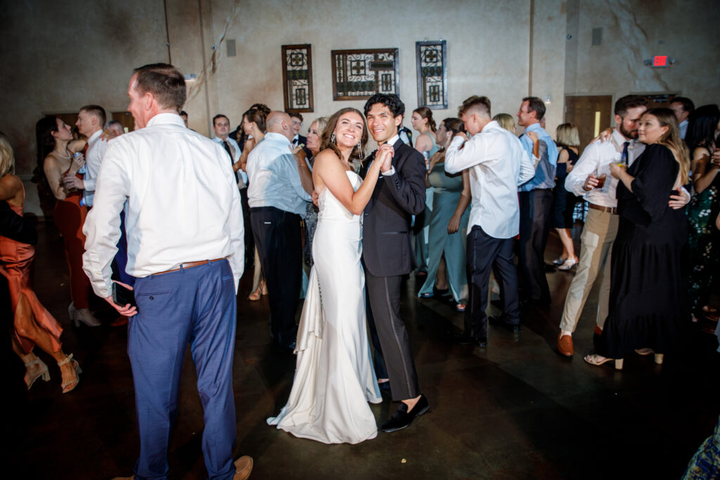 Bride and groom dancing, surrounded by guests at a wedding reception.