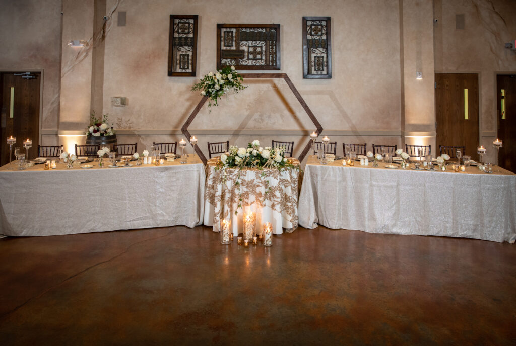 Wedding reception setup with hexagonal wooden arch, floral centerpiece, candle arrangements, and elegantly decorated tables.