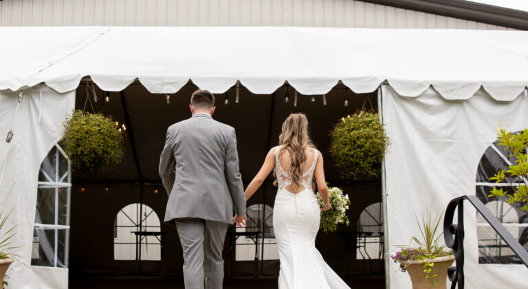 Bride and groom walking into a white tented venue on a cloudy day.