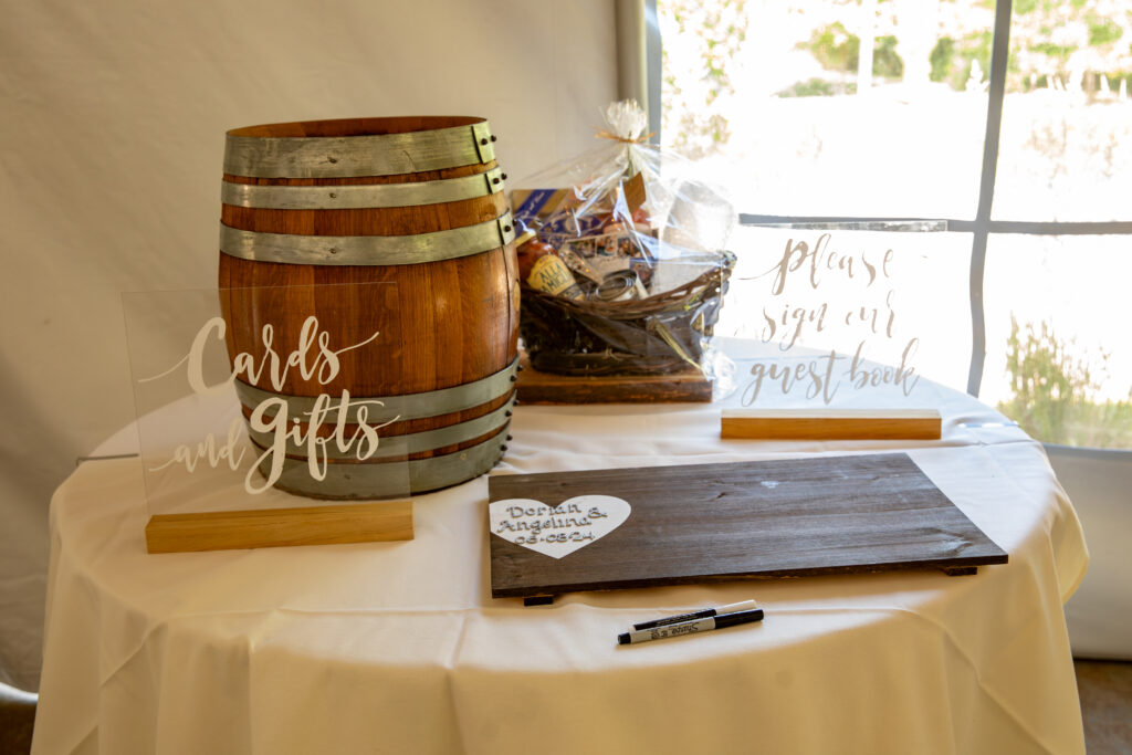 Wedding table with a barrel, a "Cards and Gifts" sign, guest book, and a pen placed on a white tablecloth.