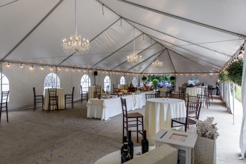 A decorated wedding reception tent with chandeliers, round tables, chairs, and a buffet setup.