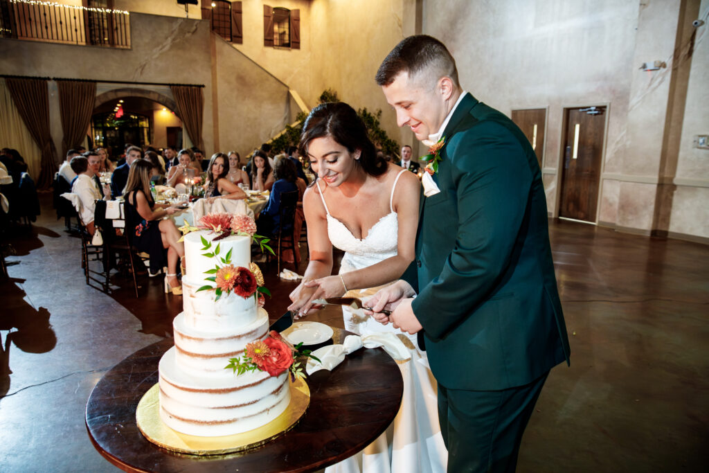 Bride and groom cut a tiered wedding cake decorated with flowers at a reception.