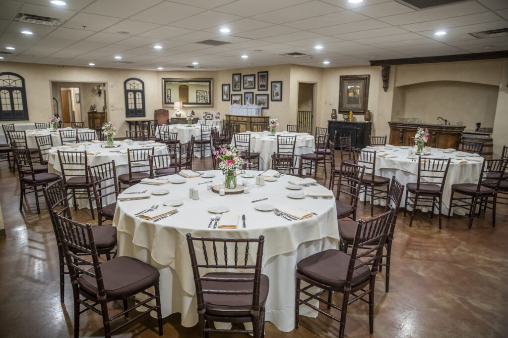 Elegant event hall with round tables set for dining, featuring white tablecloths and floral centerpieces.