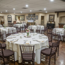 Elegant event hall with round tables set for dining, featuring white tablecloths and floral centerpieces.