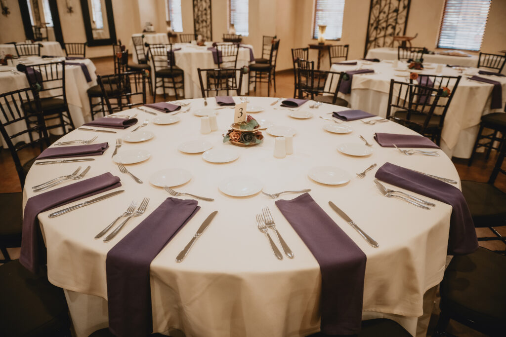 Elegant table setting with white tablecloth, purple napkins, and tableware, ready for a formal event.