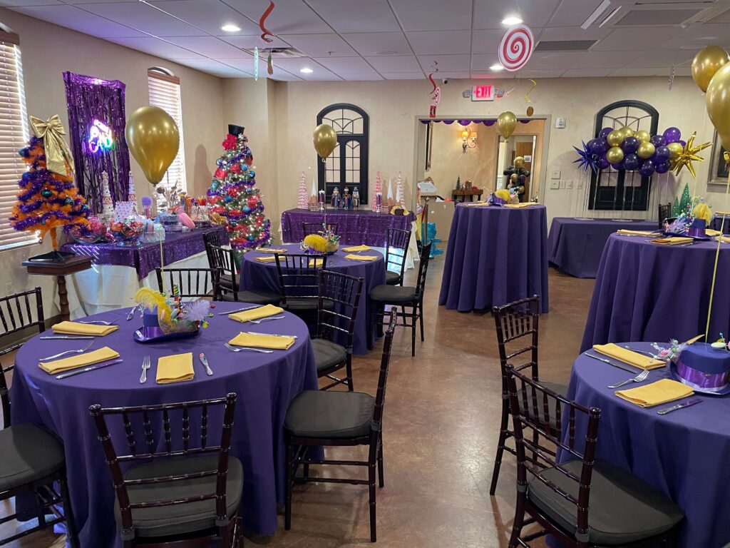 Room decorated for a party with purple tablecloths, colorful centerpieces, and festive balloons.