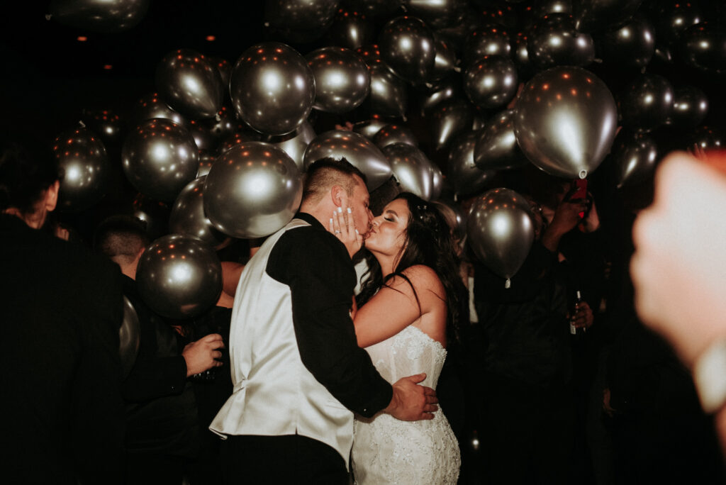Couple embracing at an event with many silver balloons in the background.