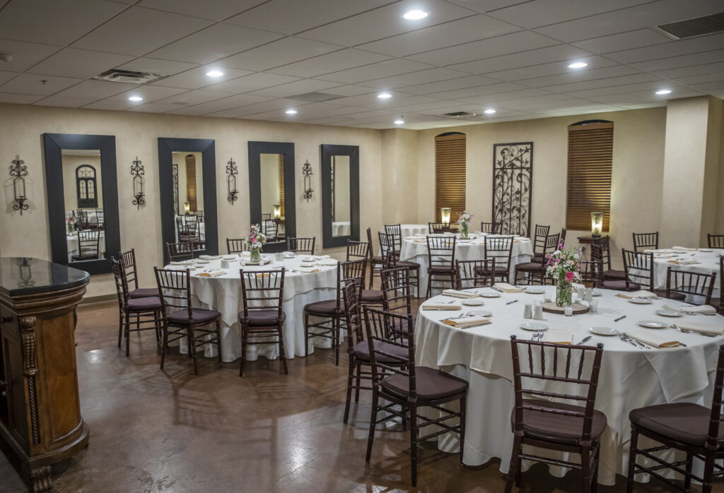 Banquet room with round tables set for a meal, featuring wooden chairs and floral centerpieces.