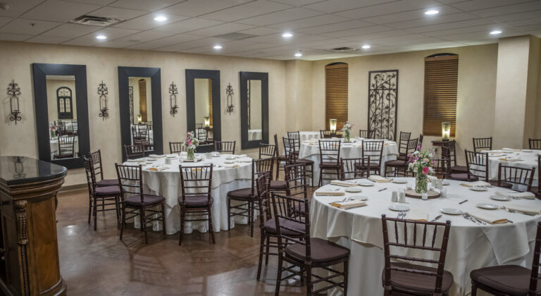 Banquet room with round tables set for a meal, featuring wooden chairs and floral centerpieces.